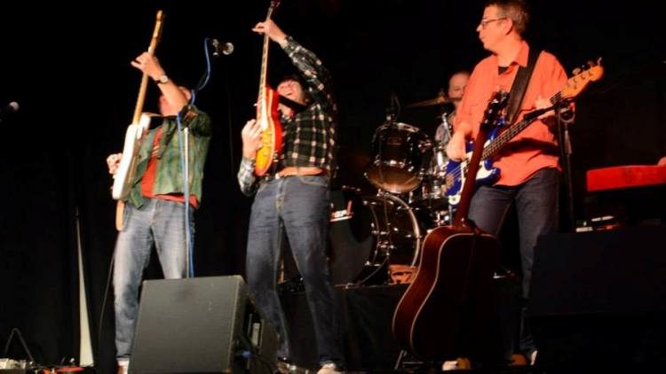Zwei Gitarristen mit hochgerissenen Gitarren, dahinter Bassist und Schlagzeuger