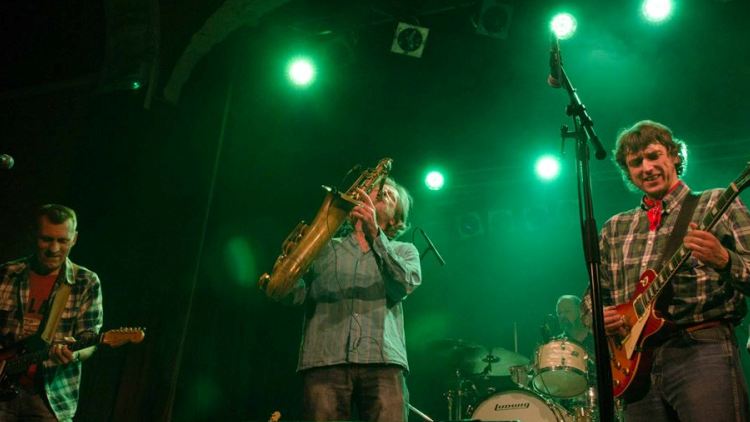 Saxophonist zwischen zwei Gitarristen in grünem Licht