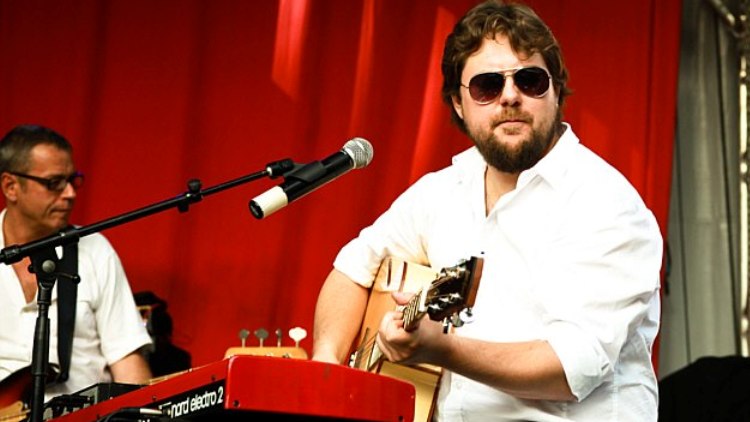 Keyboarder mit Akustikgitarre und Sonnenbrille vor rotem Vorhang