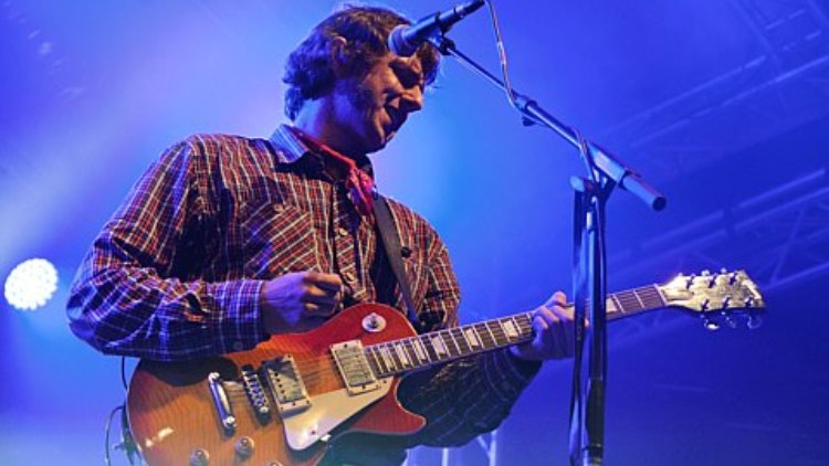 Gitarrist mit Les-Paul-Gitarre in blauem Bühnenlicht
