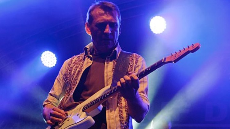 Gitarrist mit weißer E-Gitarre in blauem Scheinwerferlicht