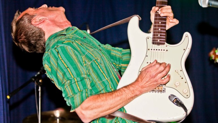 Gitarrist in grünem Hemd mit weißer Stratocaster, weit zurückgelehnt